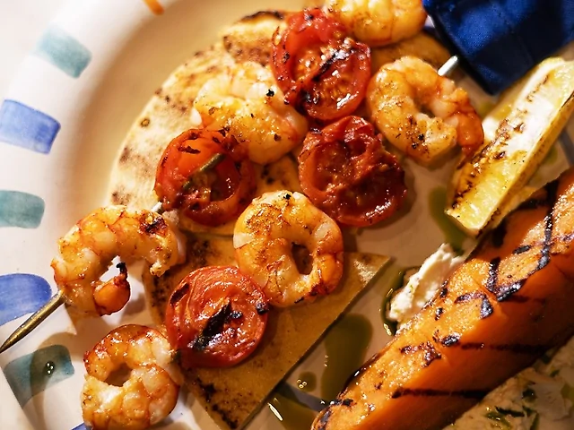 Сувлакі з лангустинів з грильованими томатами чері із запеченим бататом, пряним грецьким йогуртом та пітою